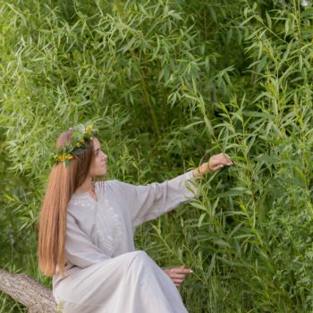 young girl in folklore dress outdoors among greenery